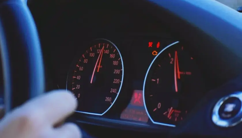 Arm am Lenkrad, Tacho zeigt 120 km/h. Warnleuchten leuchten, mögliche Motorschaden Symptome.