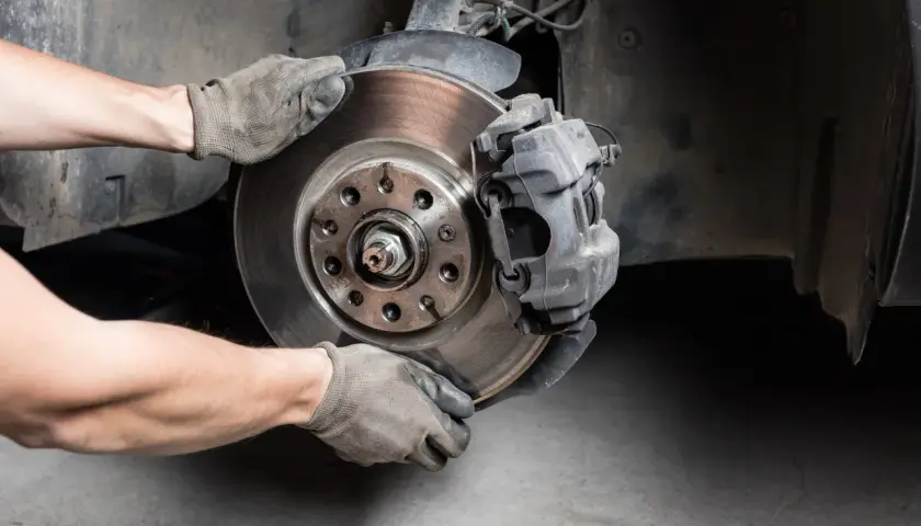 Hände in Handschuhen wechseln Bremsscheibe und Bremssattel an einem Auto.