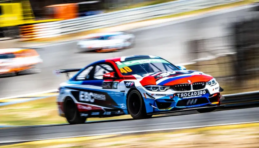 Ein BMW GT4-Rennwagen in voller Fahrt, mit lebendigen Farben und Sponsorenlogos, rast auf einer Rennstrecke.