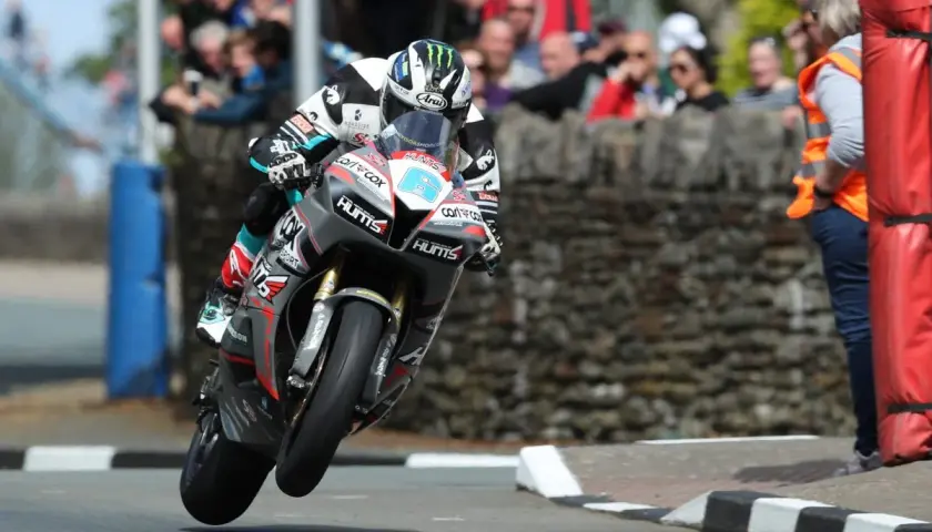 Motorradrennfahrer hebt beim Isle of Man TT ab, Zuschauer im Hintergrund.