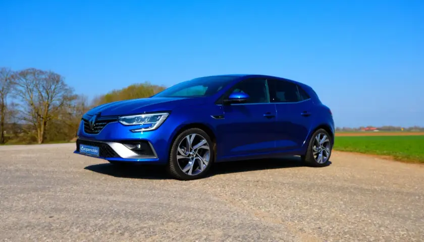 Blauer Renault Mégane 4 RS steht auf einem Feldweg vor grünen Feldern und Bäumen.