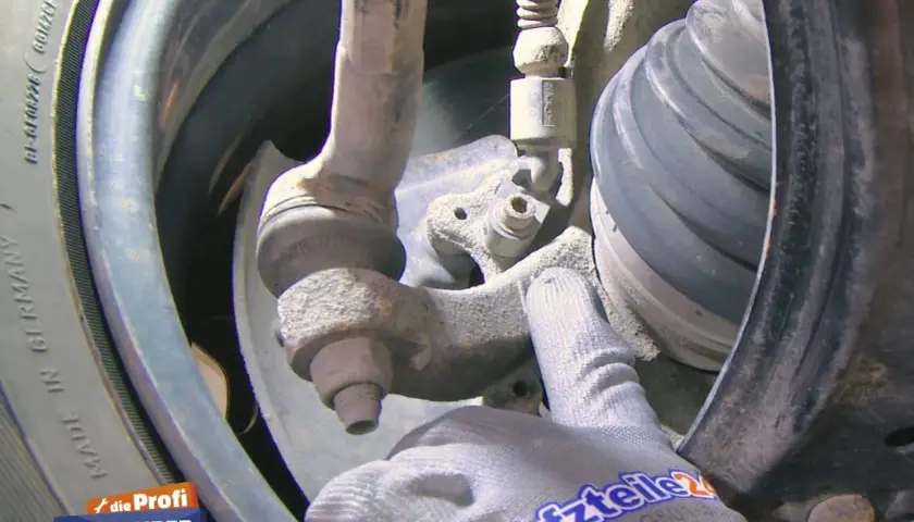 Nahaufnahme eines Audi A4 B6 Fahrwerks mit einem Handschuh, der auf den ABS-Sensor zeigt.