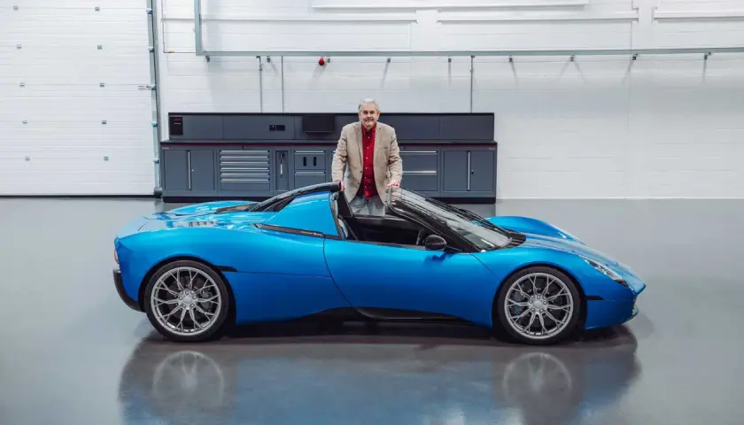 Gordon Murray präsentiert stolz seinen neuen Gordon Murray T.33, einen leuchtend blauen Supersportwagen in einer Werkstatt.