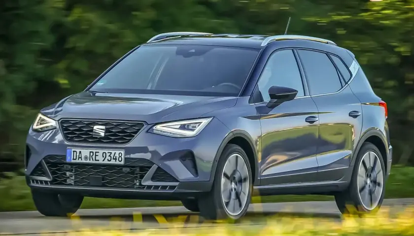 Dunkelgrauer Seat Arona fährt auf einer Straße, Bäume im Hintergrund.