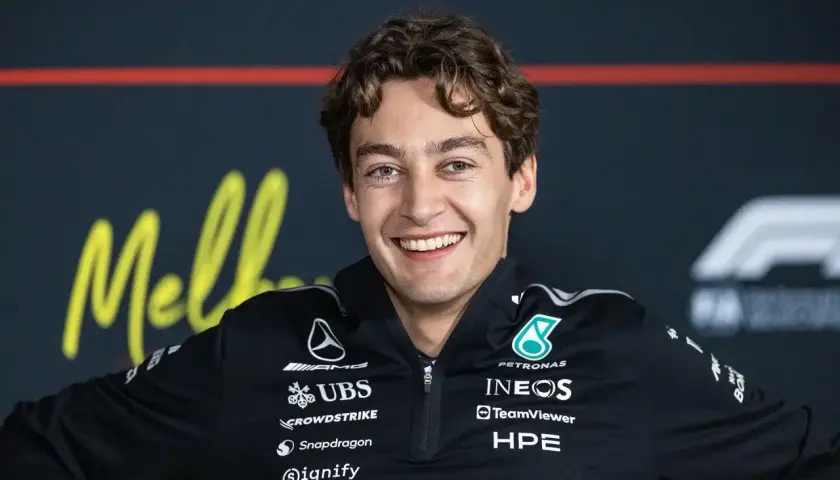 George Russell lächelt breit in seinem Mercedes-Team-Outfit. Sein Gehalt ist ein heiß diskutiertes Thema unter Fans.
