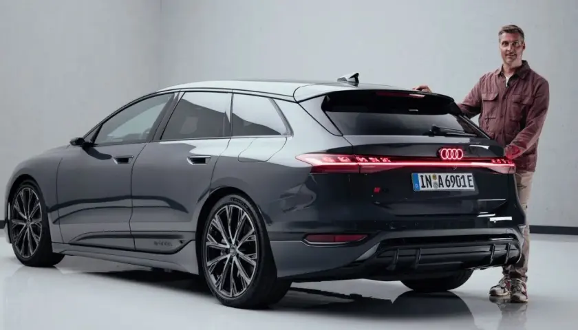 Mann steht neben dunklem Audi S6 Avant e-tron mit leuchtenden Rückleuchten.