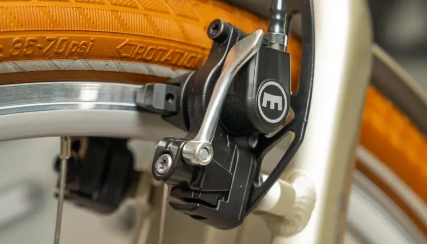 Nahaufnahme einer Fahrradbremse mit orangefarbenem Reifen und Felge.