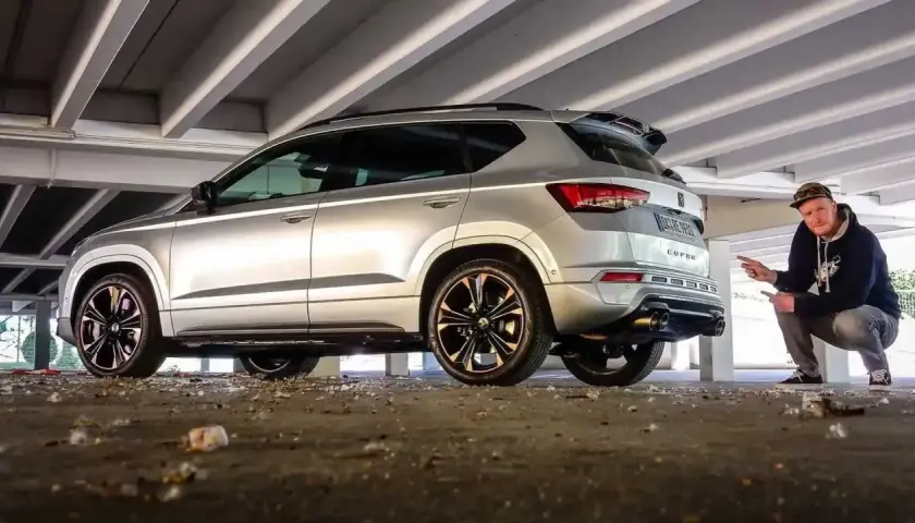 Silberner Cupra Ateca mit Mann, der auf den Auspuff zeigt, unter Betonstreben.