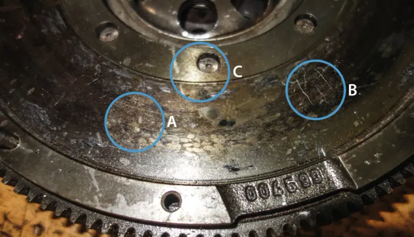 Nahaufnahme eines Zweimassenschwungrads mit markierten Verschleißspuren (A, B) und einer Schraube (C).