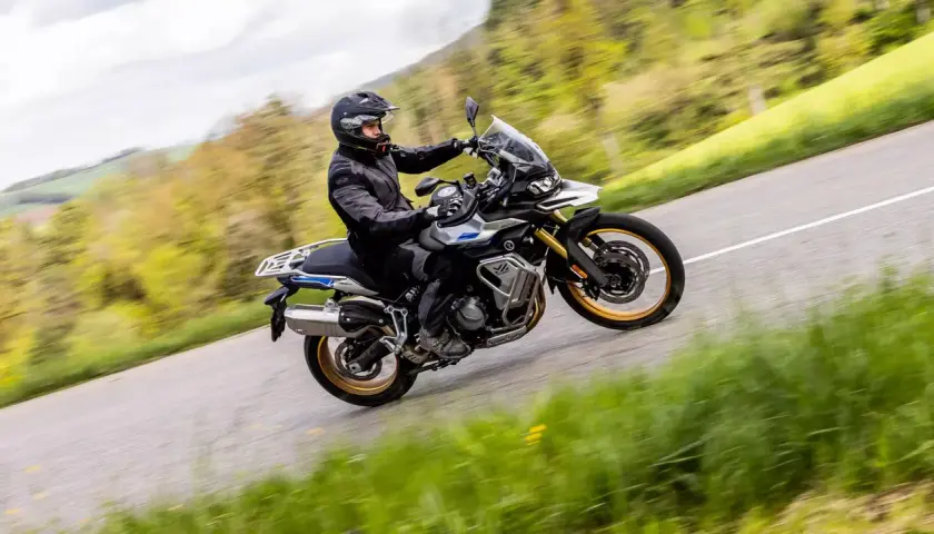 Ein Fahrer auf einer Voge DS 900 X kurvt auf einer Landstraße durch eine grüne Landschaft.