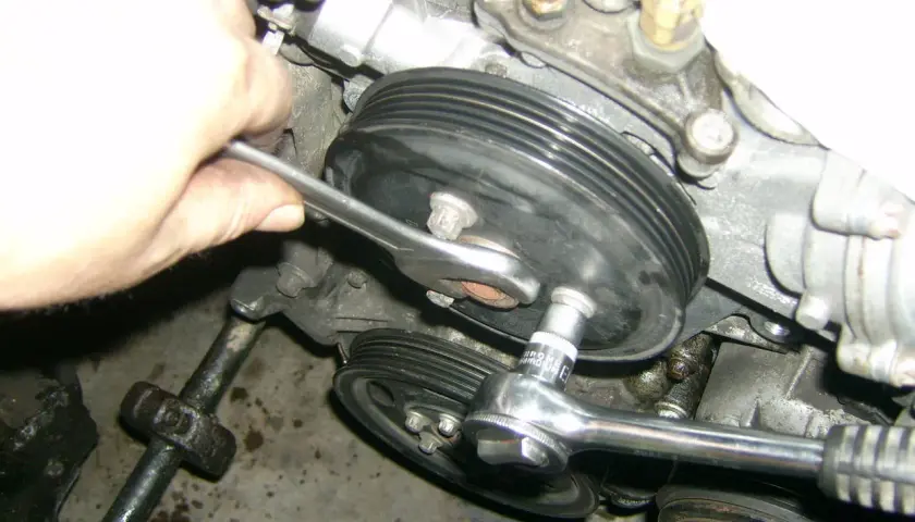 Hand mit Ratsche löst Wasserpumpenrad an einem Opel Corsa D Motor.