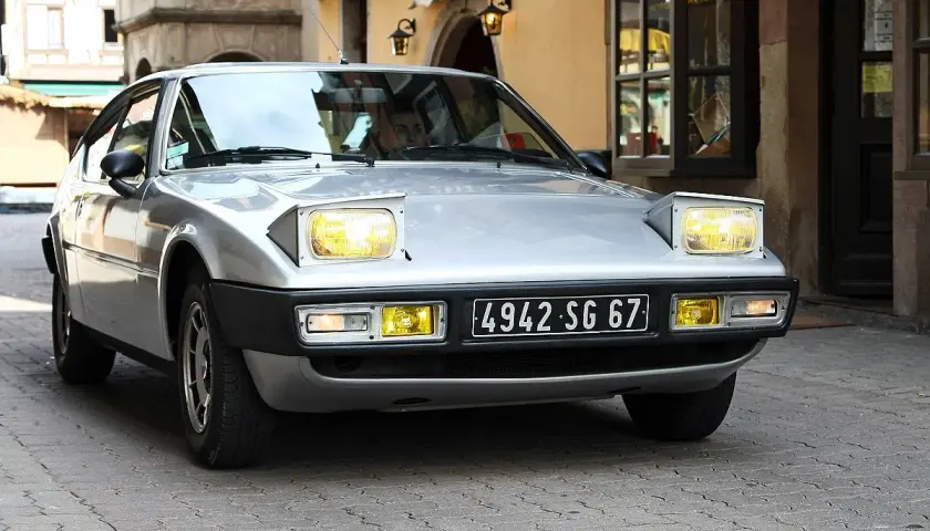 Silberner Simca Bagheera mit ausklappbaren Scheinwerfern fährt durch eine Gasse mit Kopfsteinpflaster.