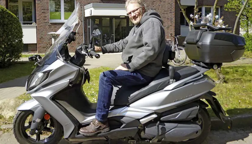 Mann auf silbernem Kymco New Downtown 350i, der über Probleme nachdenkt.