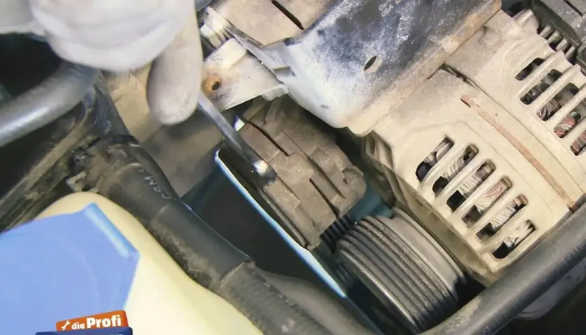 Hand mit Werkzeug am Keilrippenriemen eines Autos.