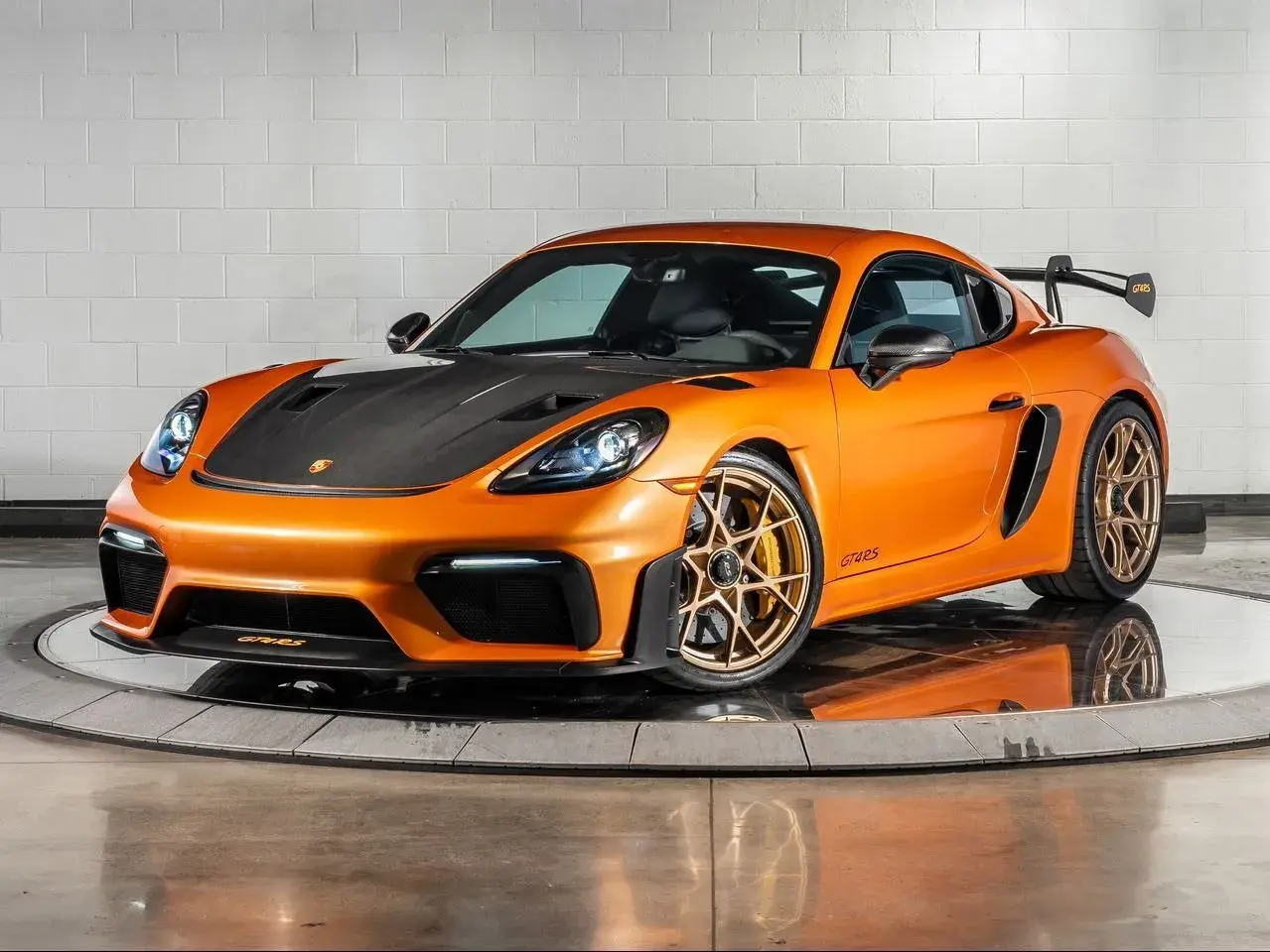 Orange Porsche GT4 RS mit Carbon-Motorhaube und goldenen Felgen, bereit für die Rennstrecke.