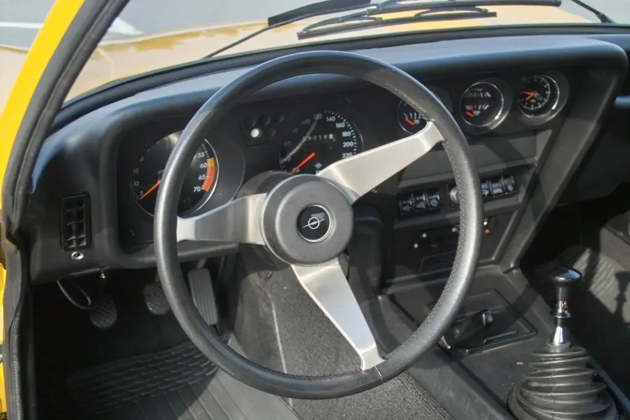 Der opel gt innenraum zeigt ein ledernes Lenkrad, klassische Rundinstrumente und einen Schaltknüppel.