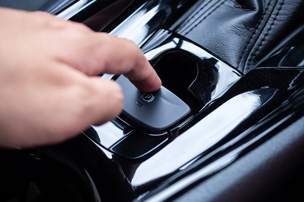 Ein Finger drückt auf den Knopf der elektronischen Handbremse. So funktioniert eine Handbremse im modernen Auto.