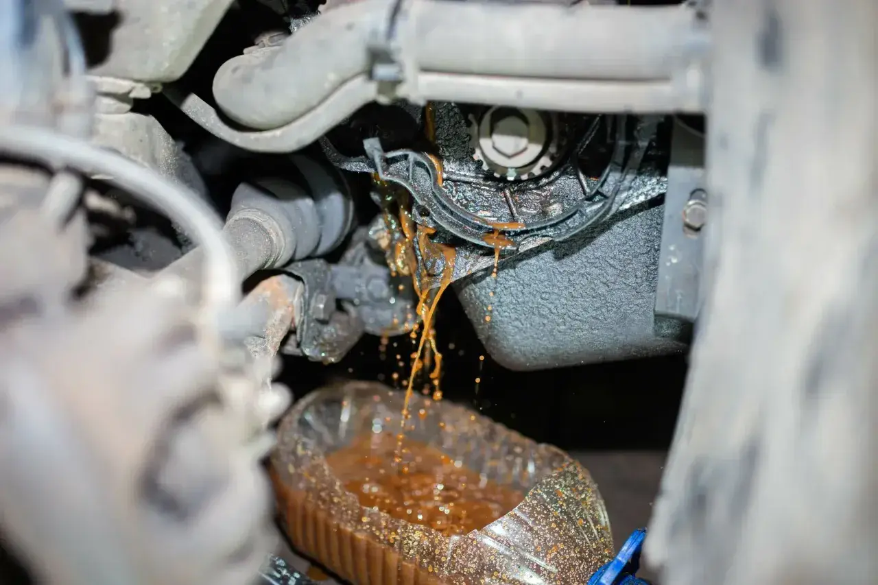 Flüssigkeit tropft aus dem Motorraum in eine Flasche. So merkt man das die Wasserpumpe defekt ist: Rostbraunes Kühlmittel tritt aus.