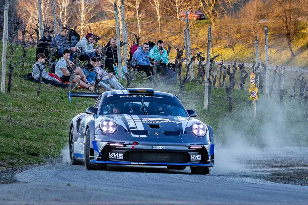 Porsche rast durch das Rebenland bei der Rallye, Zuschauer säumen die Strecke.