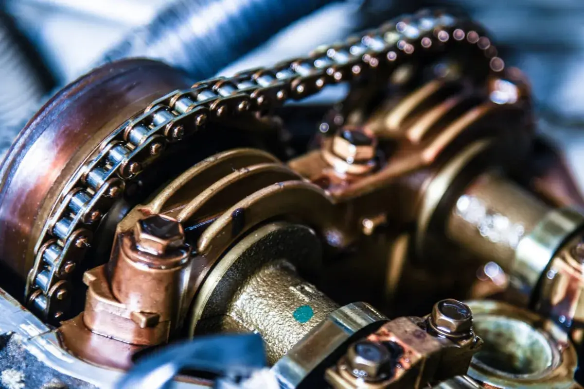 Detailaufnahme einer metallischen Steuerkette eines Autos, die über Zahnräder läuft.