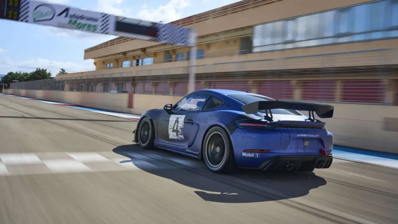 Blauer Porsche 718 Cayman GT4 Clubsport auf Rennstrecke, mit Start-/Zielbogen im Hintergrund.