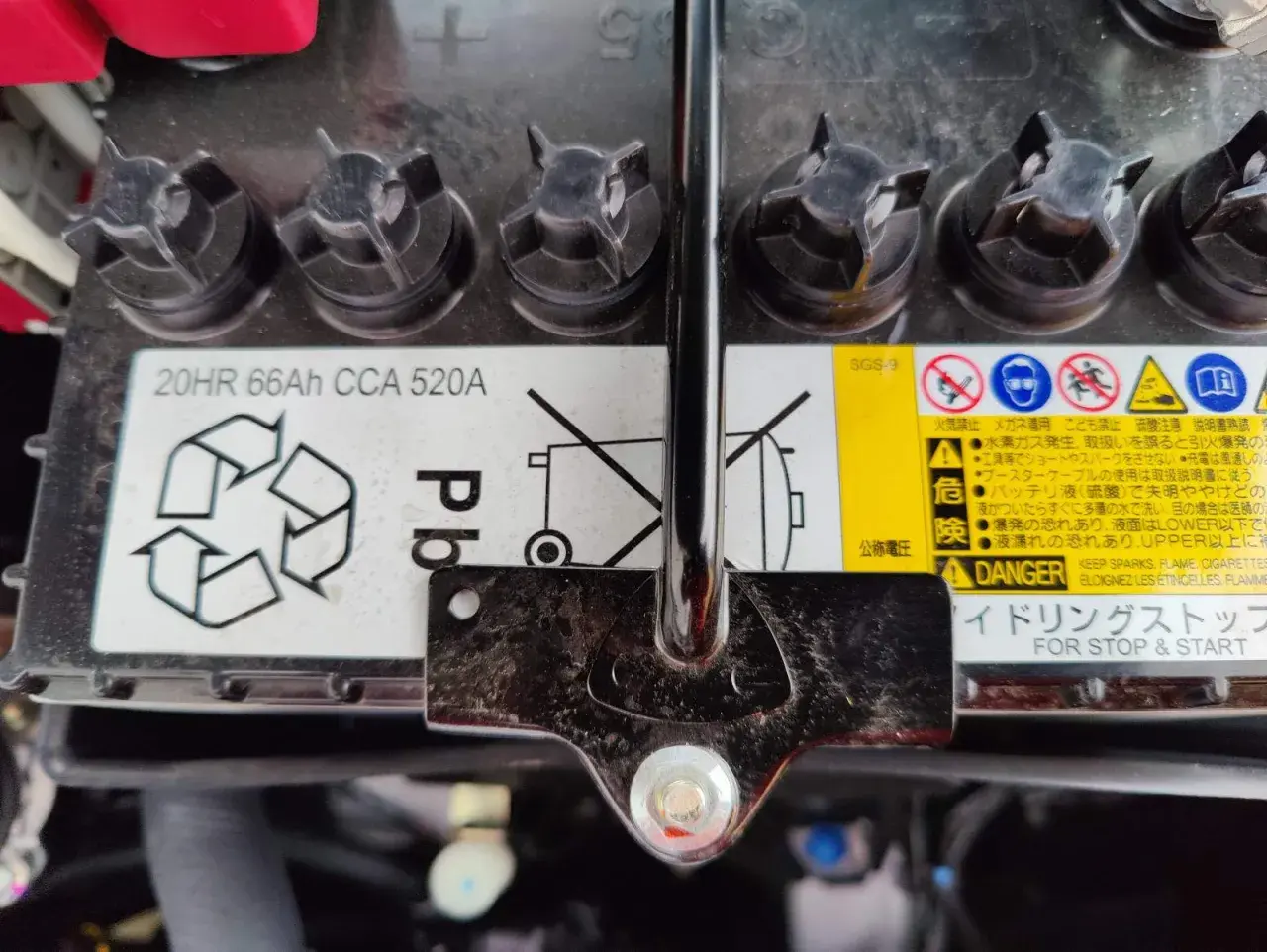 Mitsubishi Space Star Batterie wechseln: Das Bild zeigt eine Autobatterie mit Warnhinweisen und Spezifikationen wie 20HR 66Ah CCA 520A.