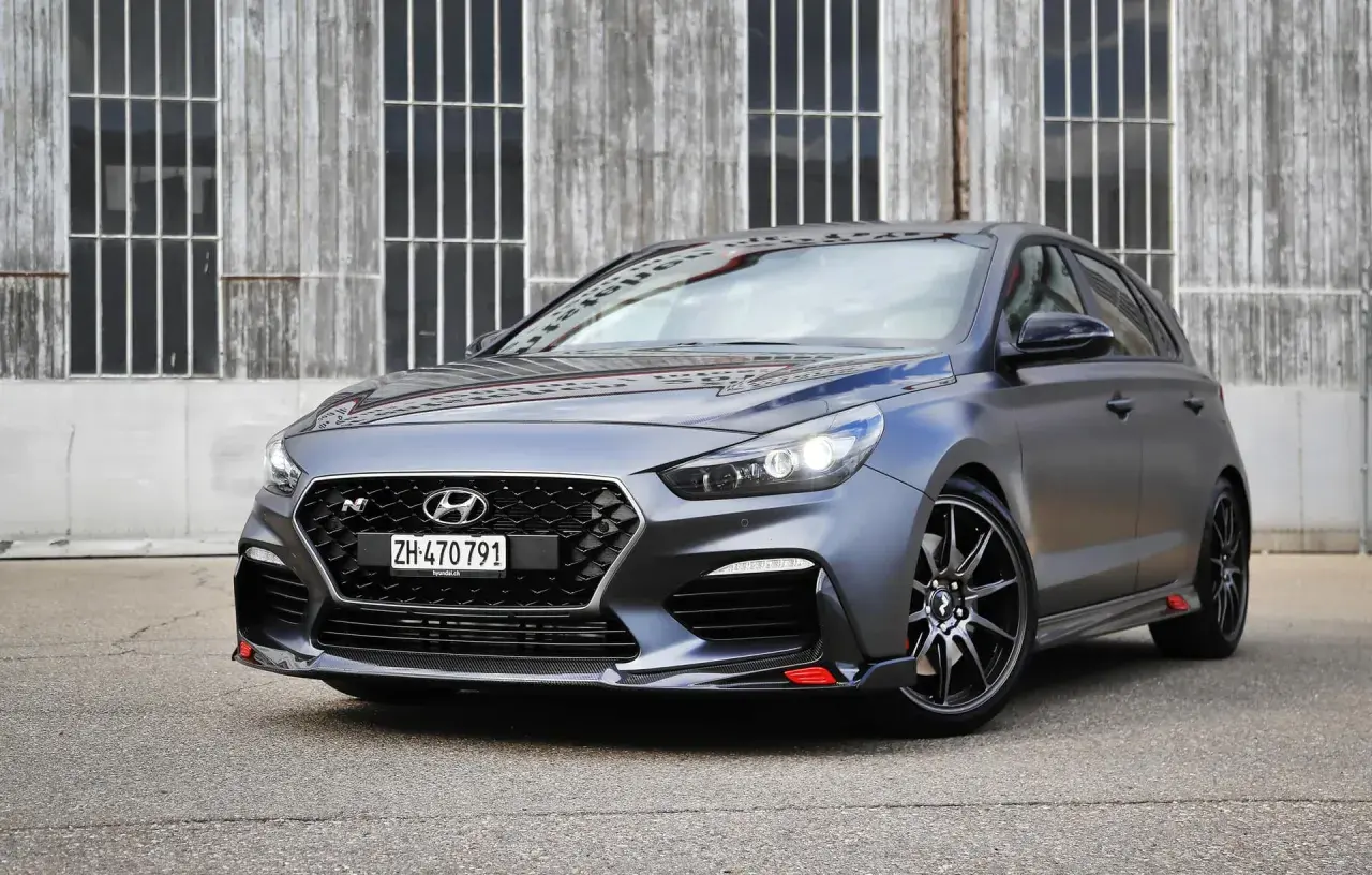 Grauer Hyundai i30 N Project C mit roten Akzenten vor Holzwand.