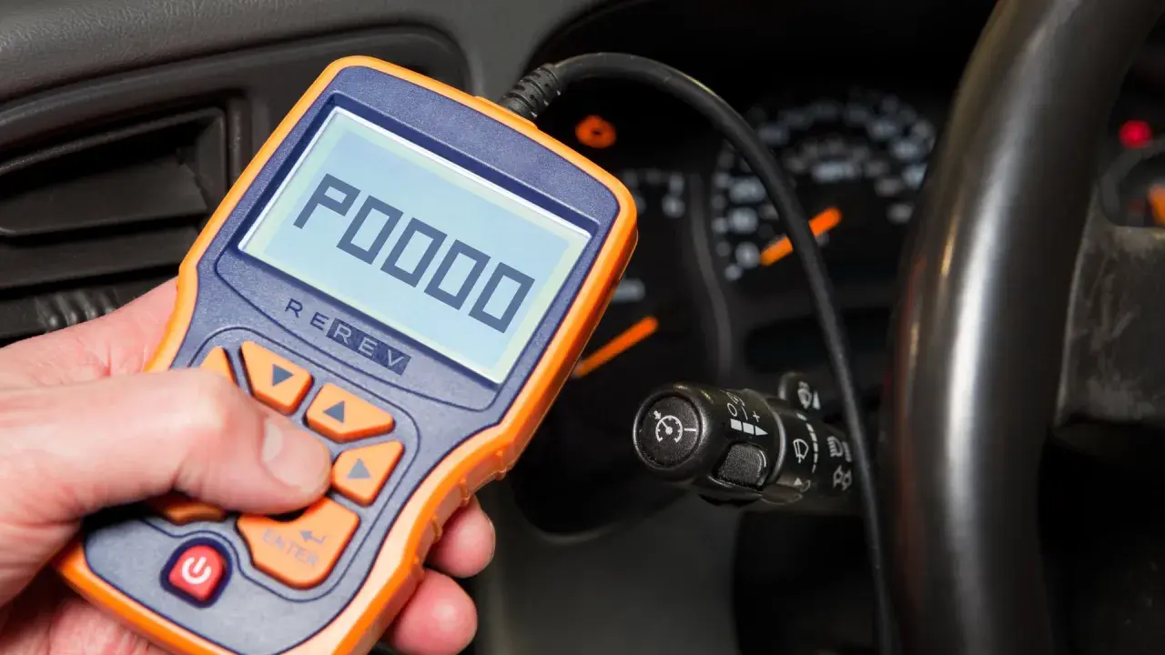 OBD-II-Diagnosegerät zeigt Fehlercode P0000 an. Ein Mann hält das Gerät in der Hand, während im Hintergrund das Armaturenbrett eines Autos zu sehen ist.