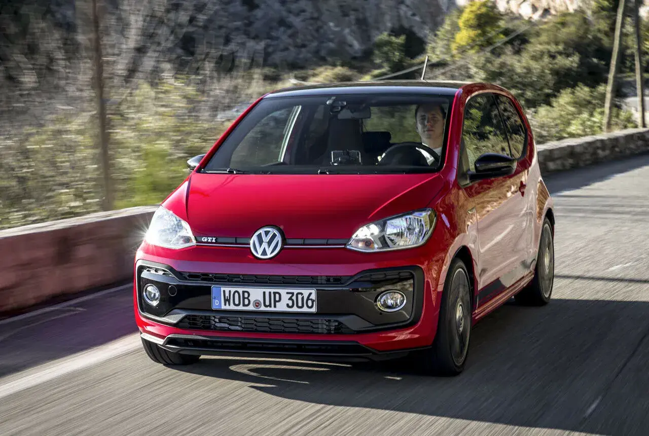 Roter VW Up GTI fährt auf einer kurvigen Straße mit Bäumen im Hintergrund.