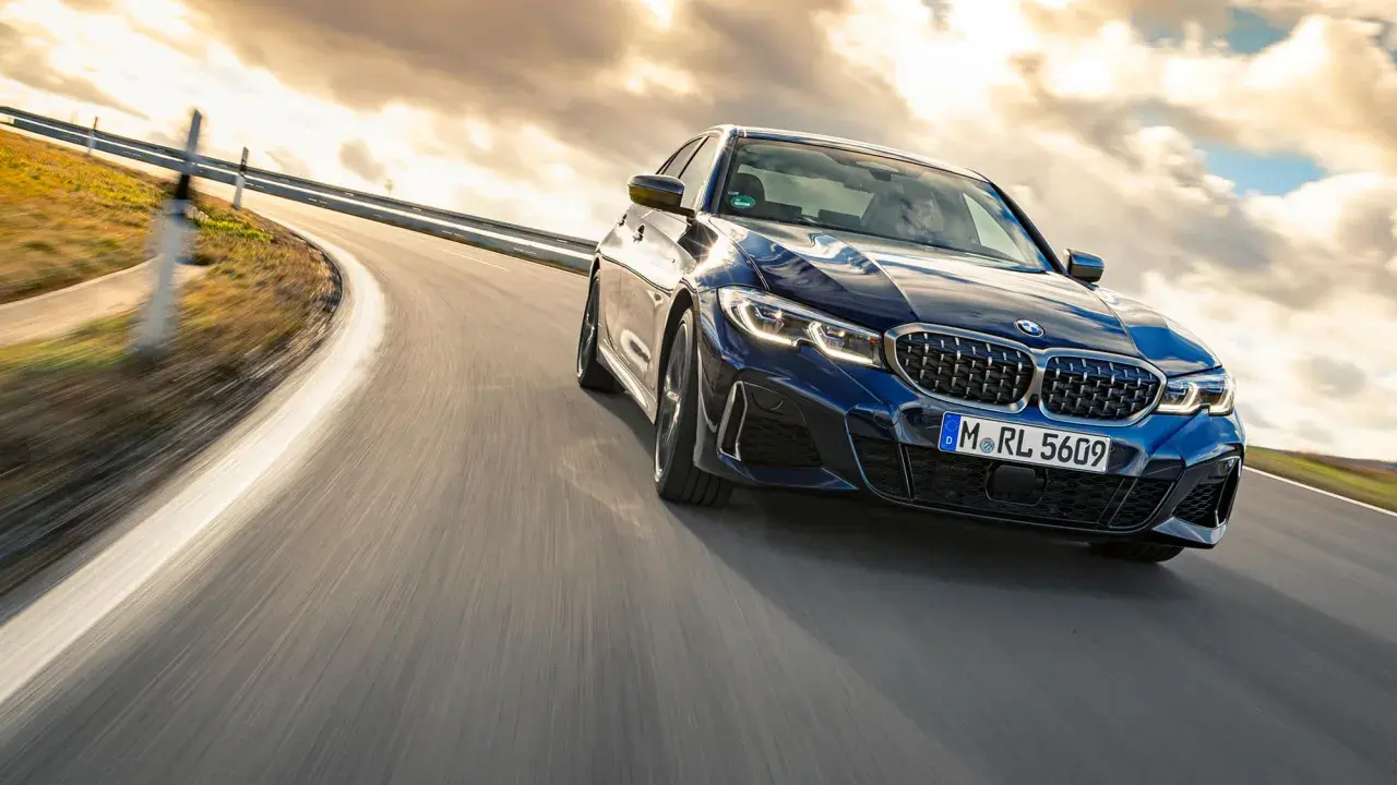 Blauer BMW M340i fährt auf einer kurvigen Straße bei Sonnenuntergang.