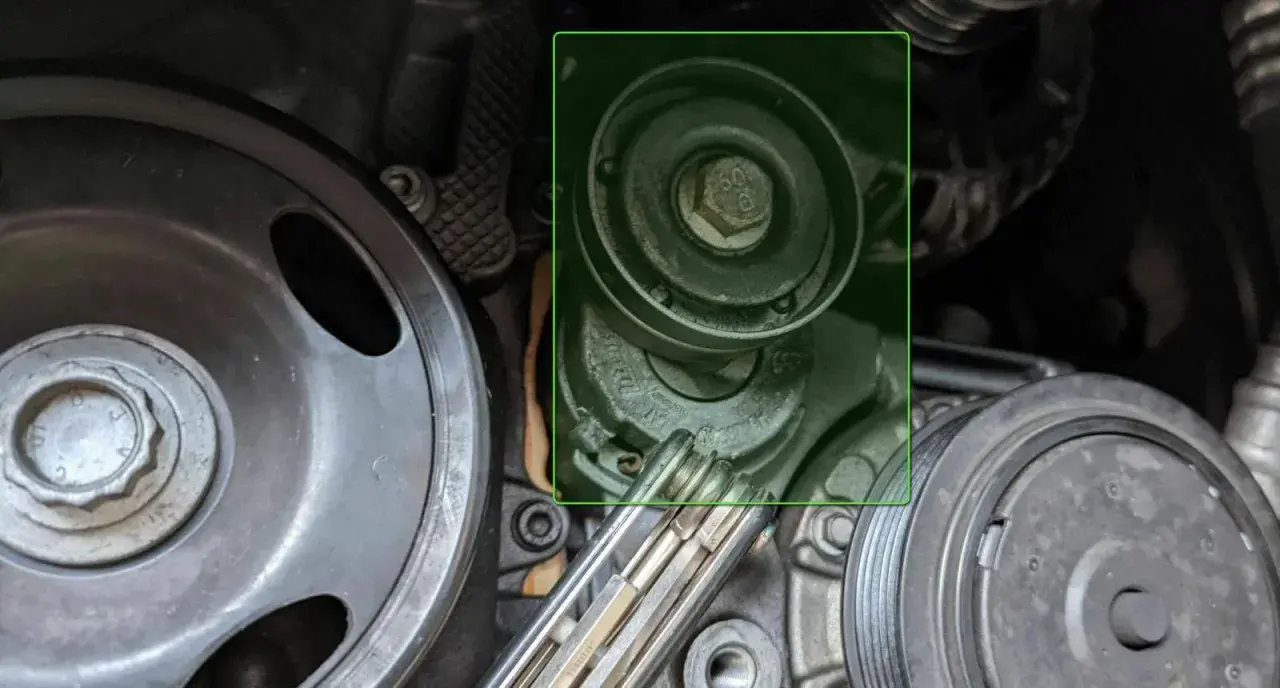 Detailaufnahme eines Keilriemenspanners und Riemenscheiben im Motorraum eines Autos.