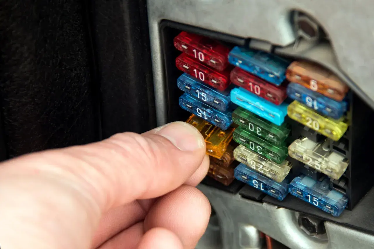 Hand prüft Sicherungen im Auto. So erkennt man eine defekte Sicherung: Der Draht im Inneren ist durchgebrannt.