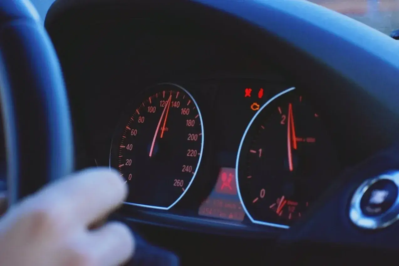 Arm am Lenkrad, Tacho zeigt 120 km/h. Warnleuchten leuchten, mögliche Motorschaden Symptome.