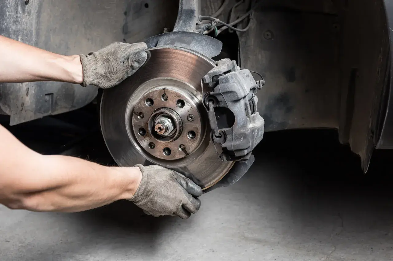 Hände in Handschuhen wechseln Bremsscheibe und Bremssattel an einem Auto.