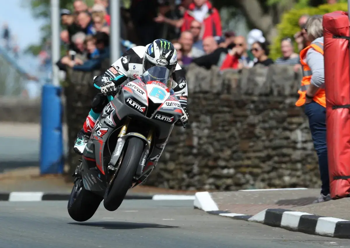 Motorradrennfahrer hebt beim Isle of Man TT ab, Zuschauer im Hintergrund.