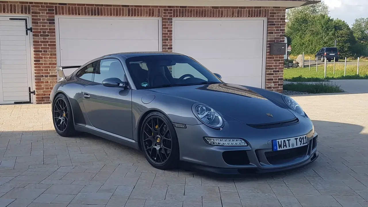 Grauer Porsche 997.1 GT3 mit schwarzem Heckspoiler und Felgen steht vor einer Garage.