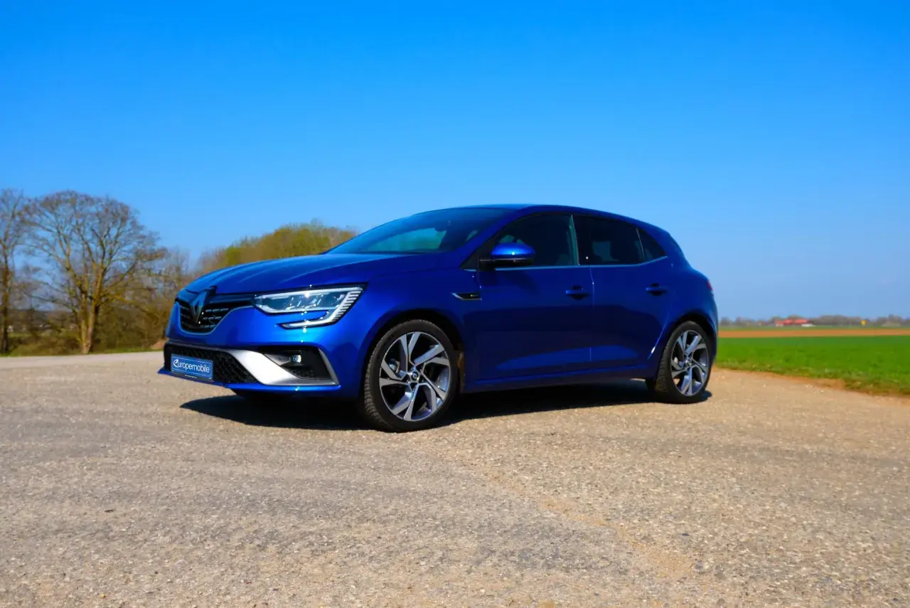Blauer Renault Mégane 4 RS steht auf einem Feldweg vor grünen Feldern und Bäumen.