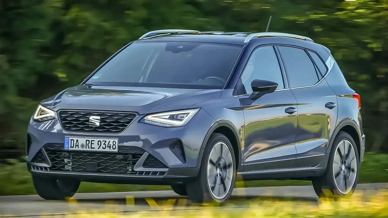 Dunkelgrauer Seat Arona fährt auf einer Straße, Bäume im Hintergrund.