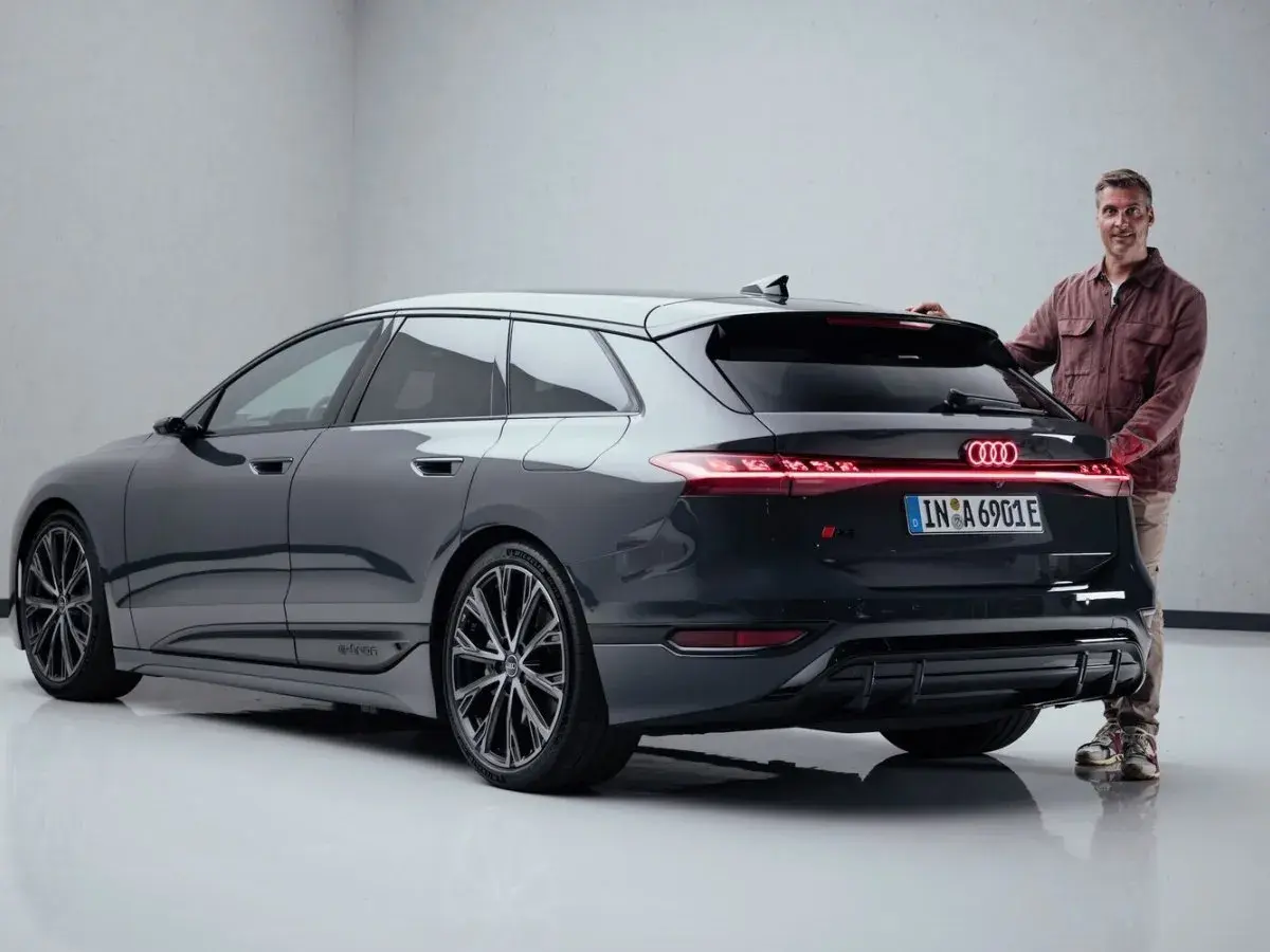 Mann steht neben dunklem Audi S6 Avant e-tron mit leuchtenden Rückleuchten.