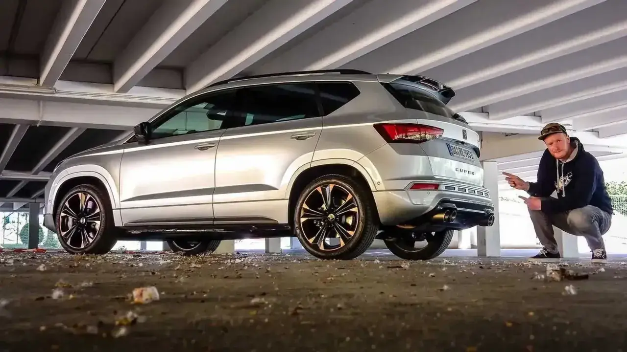 Silberner Cupra Ateca mit Mann, der auf den Auspuff zeigt, unter Betonstreben.