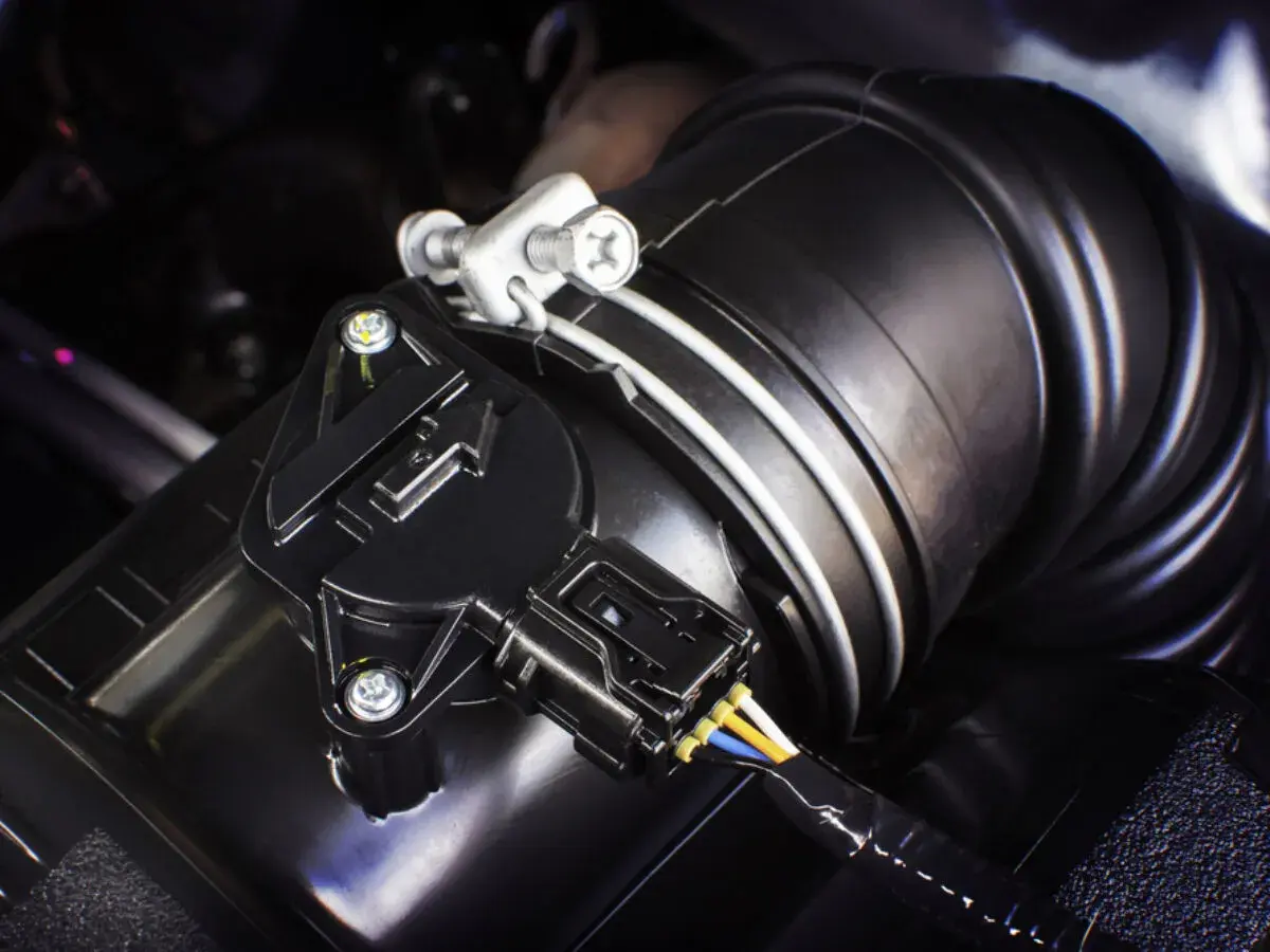 Schwarzer Ladedrucksensor mit Kabeln an einem Ansaugschlauch im Motorraum.