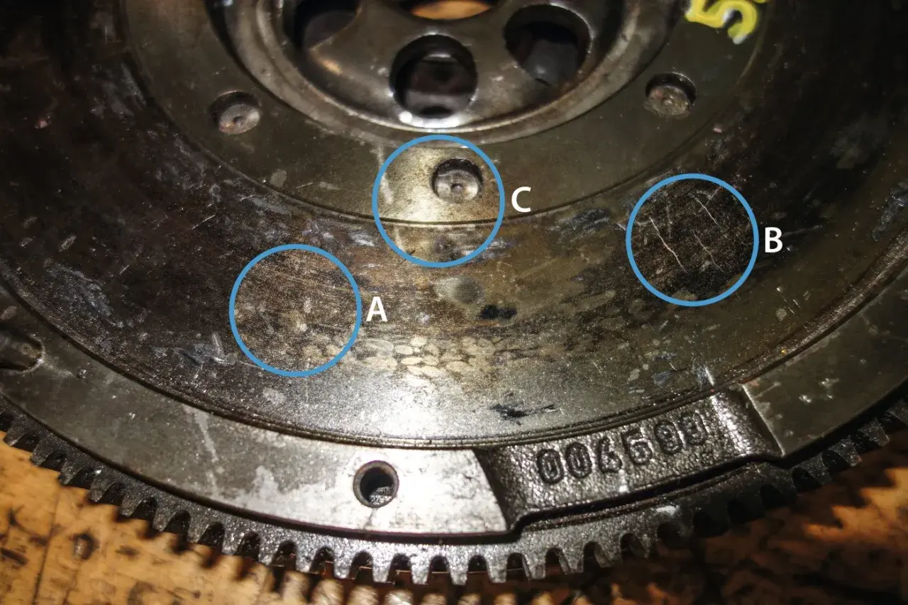 Nahaufnahme eines Zweimassenschwungrads mit markierten Verschleißspuren (A, B) und einer Schraube (C).