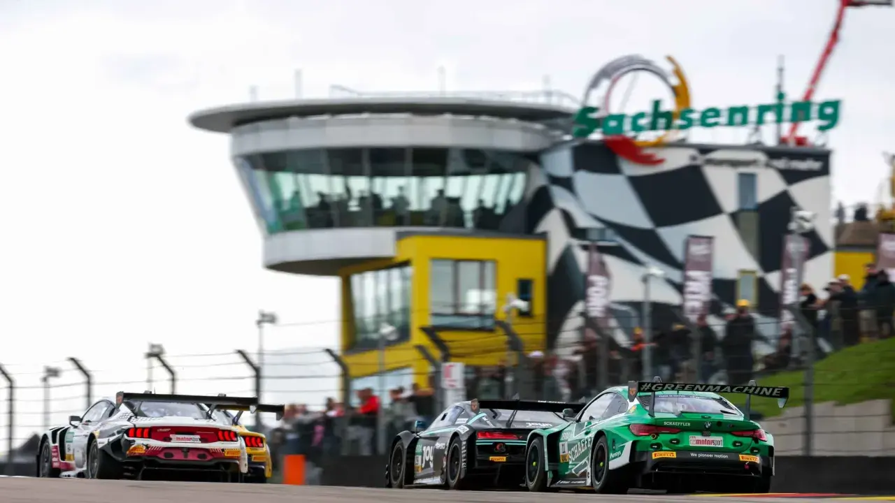 Rennwagen rasen auf dem Sachsenring. Ein grüner BMW mit #GREENMACHINE-Schriftzug und ein roter Ford Mustang liefern sich ein spannendes DTM-Rennen.