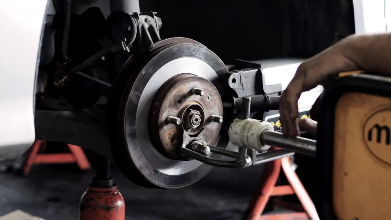 Mechaniker arbeitet an einer **Bremsscheibe**. Das Auto steht auf einem Wagenheber.