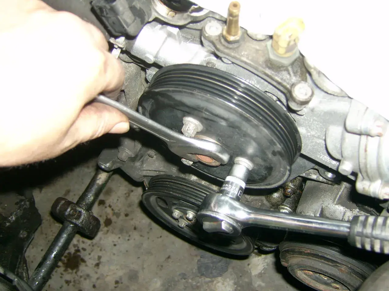 Hand mit Ratsche löst Wasserpumpenrad an einem Opel Corsa D Motor.