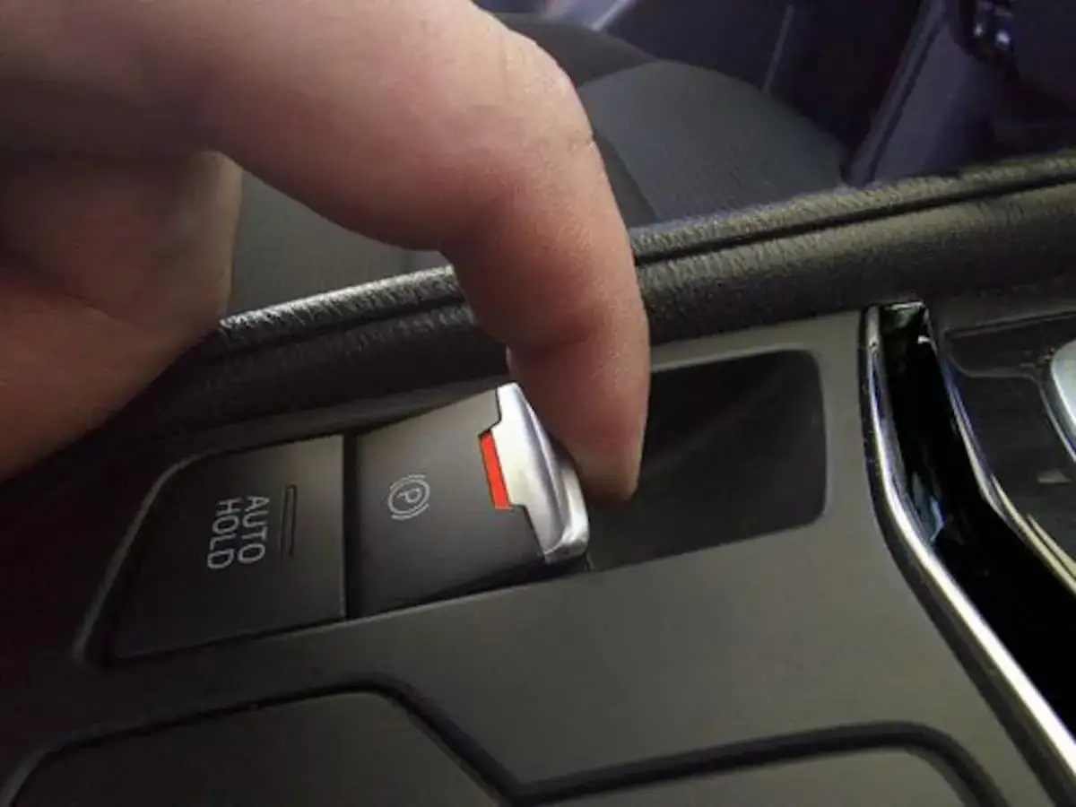 Finger drückt den Knopf für die elektronische Parkbremse. Ein rotes Licht zeigt an, dass das Auto bremst, falls es nicht mehr bremst.
