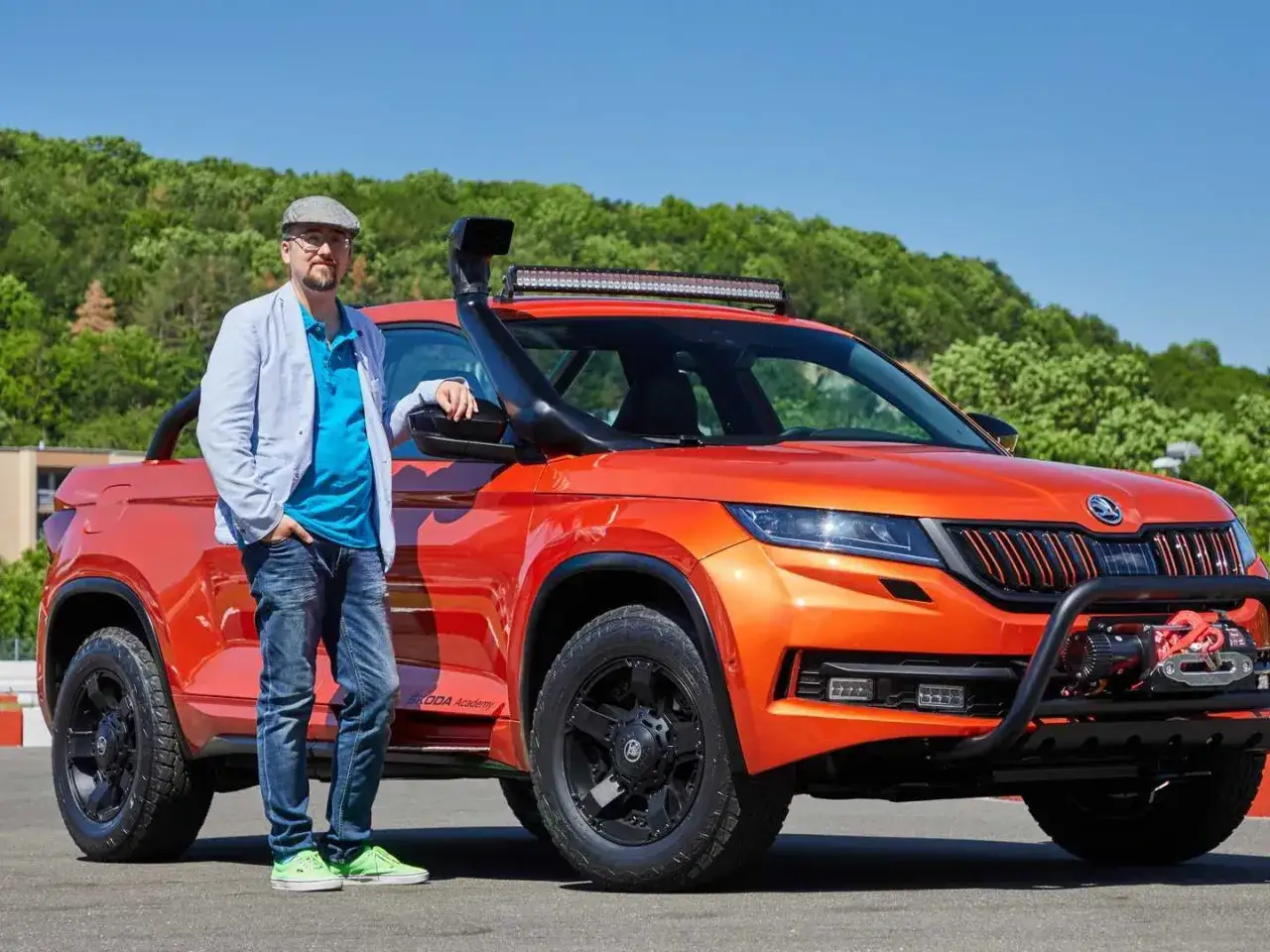 Ein Mann steht neben einem orangefarbenen Skoda Mountiaq mit Schnorchel und Seilwinde, bereit für jedes Abenteuer.