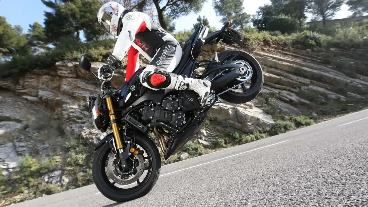 Motorradfahrer im Stunt, das Vorderrad in der Luft. Der Bremsweg des Motorrads ist hier irrelevant, da er gerade einen Wheelie macht.