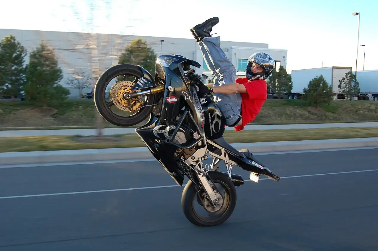 Motorradfahrer macht einen spektakulären wheelie, wobei das Vorderrad in der Luft ist.