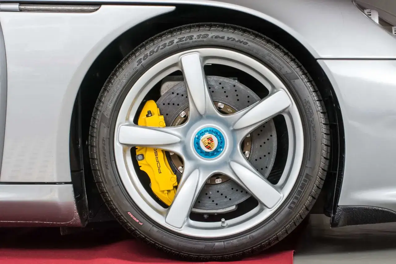 Silbernes Porsche-Rad mit gelben PCCB-Bremsen und Porsche-Logo.